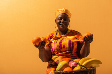 smiling middle aged african american saleswoman sitting near fruits on orange