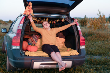 A cheerful and funny baby boy sits in the trunk of a car decorated with decor in honor of the autumn holiday Halloween, holding a bouquet of orange color. Lifestyle.