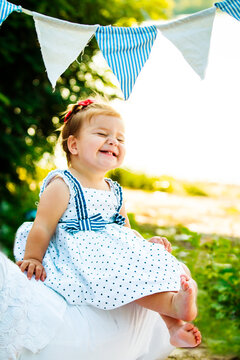 The little girl is smiling sincerely screwing up his eyes. The child crossed feet. Little feet todder who had just started to walk. A child rests on the coast.