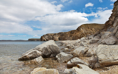 Baikal Lake in summer. A beautiful landscape of the coast of Olkhon Island with large smooth stones on a sandy beach in a shallow bay. Natural background. Travel and hikes around the island