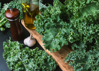 Bunch of raw curly kale on a wooden cutting board, olive oil, pepper and garlic.