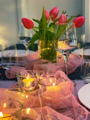 Wine glass detail on romantic dinner table decorated with red tulips and candles.