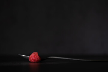 Red ripe raspberries on a spoon shot against a light/dark background with space for text
