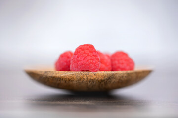 Red ripe raspberries on a spoon shot against a light/dark background with space for text
