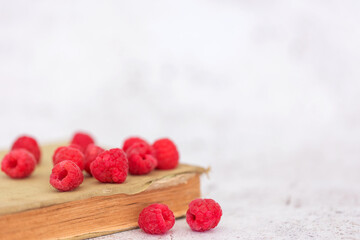 ripe raspberries shot against a light coloured background, wooden bowl, white china heart mug