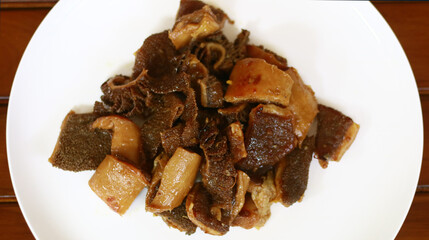 Braised beef tripe or bacem babat on white plate, wood background.