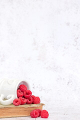ripe raspberries shot against a light coloured background, wooden bowl, white china heart mug