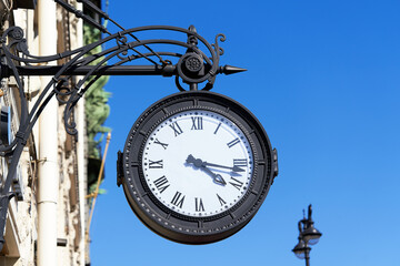 Fototapeta na wymiar Antique round clock with Roman numerals hang on the street of the city