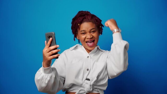 Successful afro woman recieved good news on smartphone and clenches fist, achieved her goal