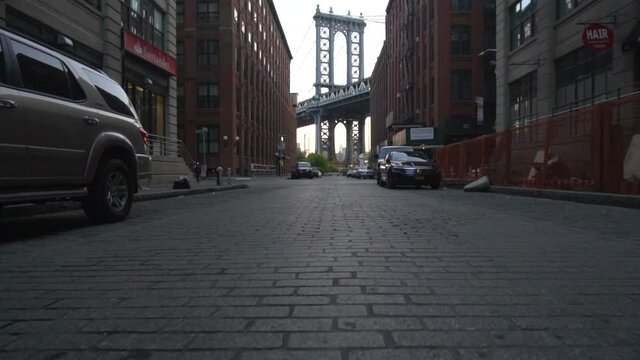 Brooklyn Bridge View from Dumbo with dumbo apartment houses and parked cars on the side in Summer in early morning light 