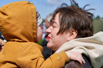 Fototapeta premium Mom with short hair kisses her little son while holding him in her arms