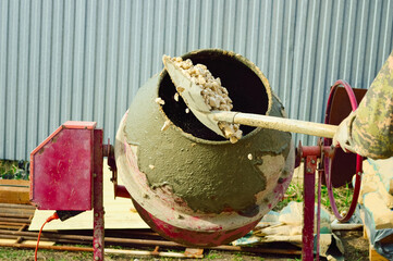 close-up - a worker throws rubble with a shovel into a concrete mixer to make mortar