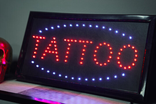 Illuminated signboard with neon word tattoo on shelf near decorations