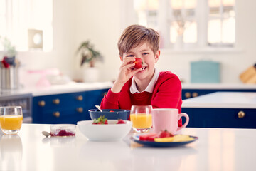 Obraz na płótnie Canvas Laughing Boy Wearing School Uniform In Kitchen Eating Healthy Breakfast With Fresh Strawberry