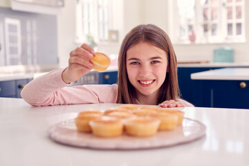 Portrait Of Teenage Girl Taking Freshly Baked Homemade Cupcake From Plate In Kitchen At Home