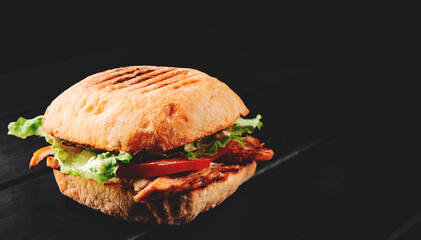 italian ciabatta panini sandwich with chicken, cheese and tomato on black wooden table