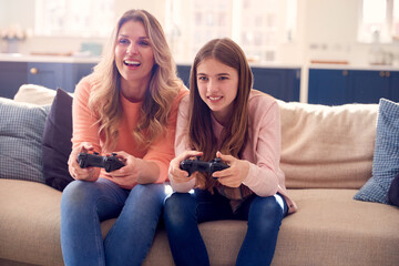 Mother And Daughter Having Fun Sitting On Sofa At Home Playing On Games Console