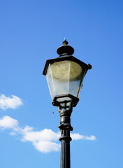 Fototapeta na wymiar Old black metal street lamp. Blue sky with clouds in the background.