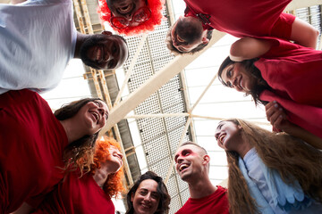Obraz premium View from below of a group of people celebrating together and hugging while cheering for their sports team from a stadium. Cheerful fans watch the game in costume at the stadium.