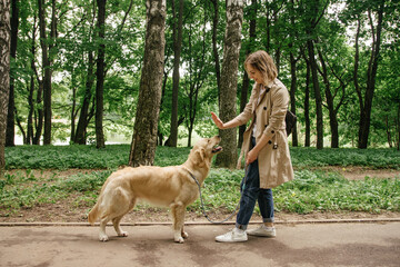 The hostess girl walks in the park with her golden retriever dog in good summer weather
