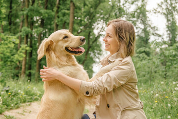 The mistress girl in the woods on the path hugs her dog of the Golden Retriever breed