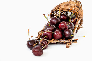 Overturned wicker basket with ripe sweet cherries spilling out of it on white background
