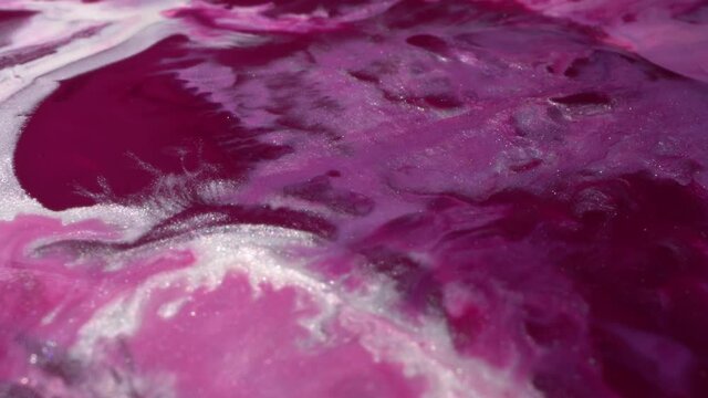 Purple, pink and shiny white pearl colors mix. Paint texture macro. Ink flow. Glitter fluid motion. Moving flowing stream of liquid paint. Beautiful abstract background