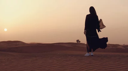 Gordijnen Portrait of a young Arab woman wearing traditional black clothing during beautiful sunset over the desert. © skymediapro