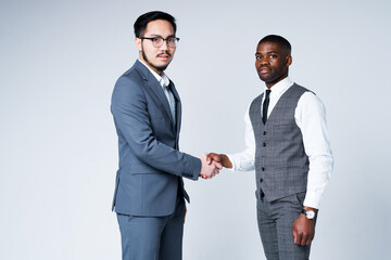 African American manager and Asian businessman shake hands with each other as a sign of truce while...