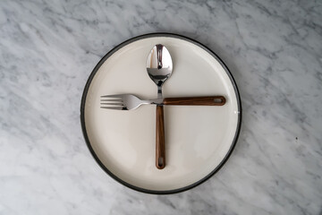 Spoon and fork forming a plus sign on an empty plate on a marble table.