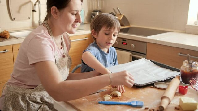 Little boy helping mother putting biscuits on baking sheet. Children cooking with parents, little chef, family having time together, domestic kitchen.