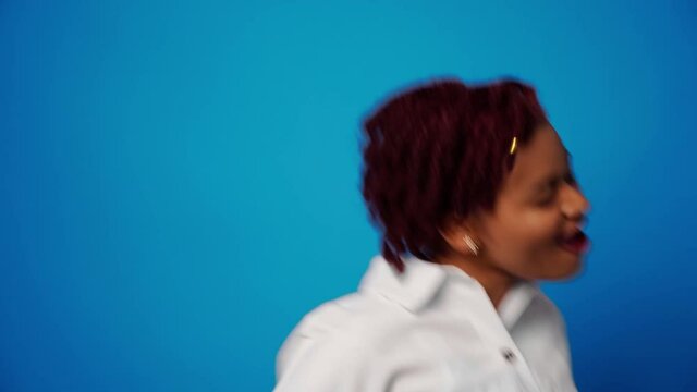Happy young afro american woman dancing in studio against blue background