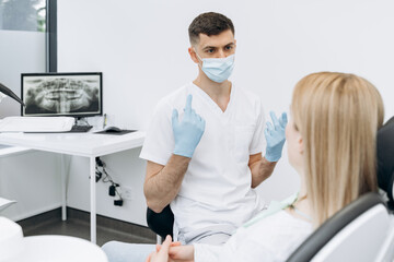 Attractive dentist in a protective mask communicates with an attractive patient. The dentist works in the dental office