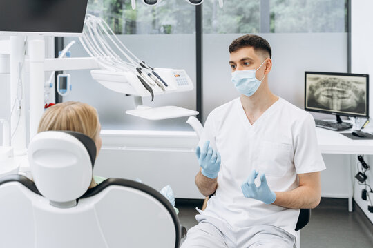 Dentist in a protective mask explains to the patient. The dentist works in the dental office