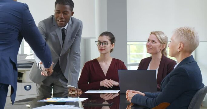 Close up of boss handshaking african american worker at corporate group meeting