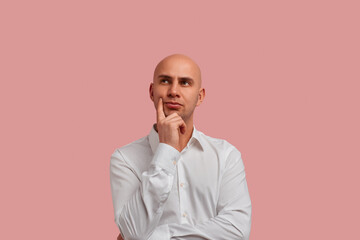 Gifts or vacation. Serious brooding bald man in white shirt holds chin and looks confused. Thinks what to do with holidays. Isolated over pink background.