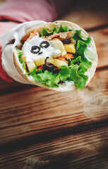 greek meat gyros with tzatziki sauce, vegetables, feta cheese and french fries in woman hand. street food