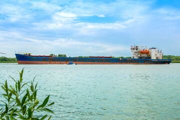 A large cargo ship is anchored in the river. Big ship and small boat