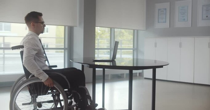Positive disabled young man in wheelchair working in office