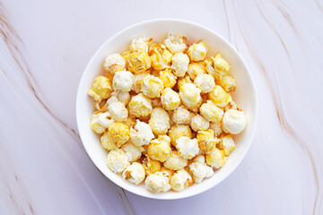 A small white bowl of caramelized popcorn. Light marble background. Sweet popcorn close up.