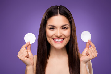 Portrait of attractive cheerful woman holding in hands cotton pads isolated over bright violet purple color background