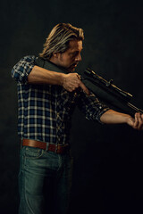 Fototapeta premium Man with blond hair in lumberjack shirt and jeans aims a shotgun.