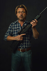 Man with blond hair in lumberjack shirt and jeans is holding a shotgun.