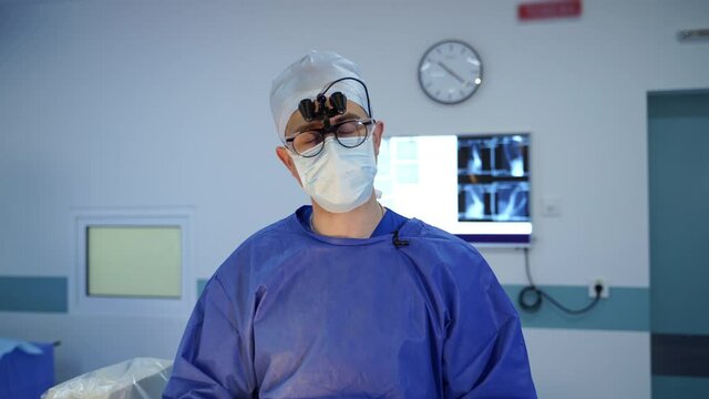Portrait of a doctor talking on camera. Neurosurgeon using glasses with microscope lenses telling about health problems in the operating room.
