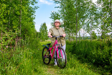 Naklejka premium Grandma rides a bike. An elderly woman rides a bicycle in nature.
