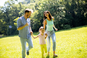 Happy young family with cute little daughter running in the park on a sunny day