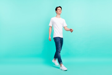 Fototapeta na wymiar Full length profile photo of funny brunet hairdo teenager guy go look empty space wear t-shirt jeans isolated on teal background
