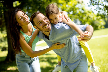 Happy young family with cute little daughter having fun in the park on a sunny day