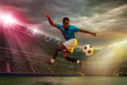 Goal. Male african socce, football player jumping in attack during sport match on cloudt sky background at stadium