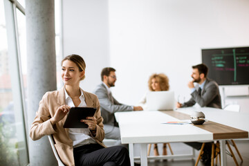 Young woman sitting by the table with digital tablet in modern office in front of her team